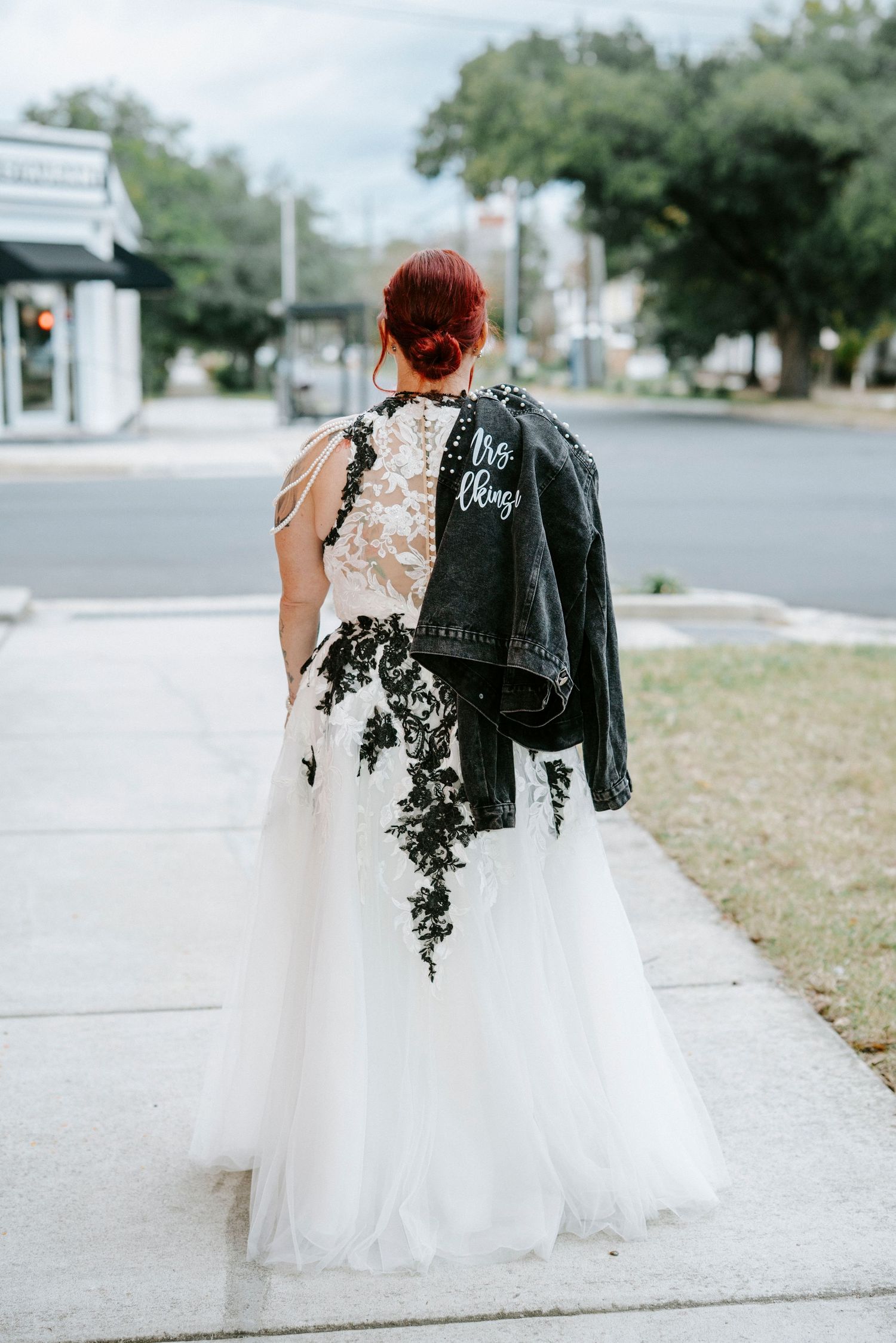 A couple in contrasting black leather and white tulle wedding attire walking together on a street.