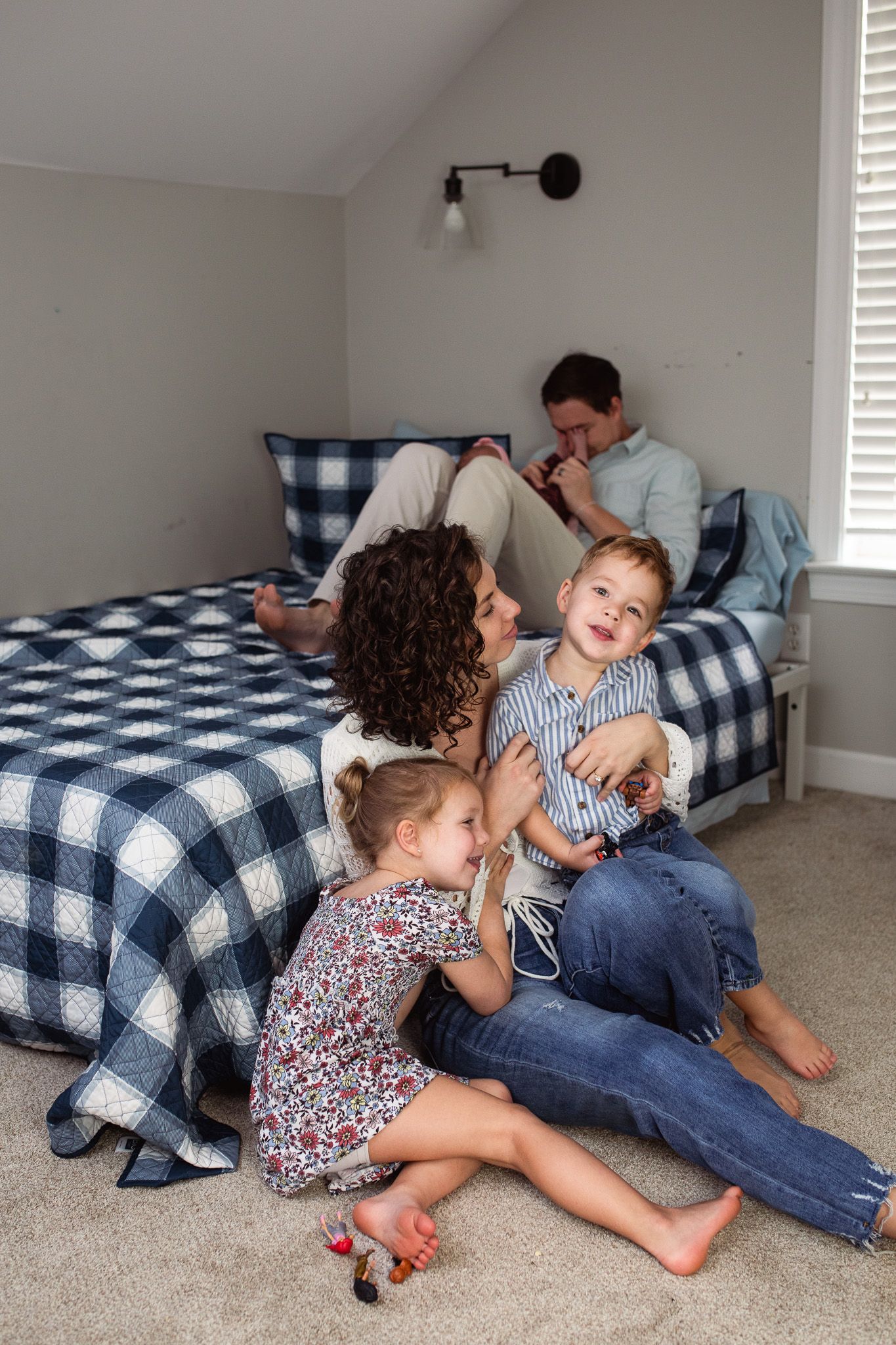 A playful moment captured showing joyful interaction on a carpeted floor with blue plaid bedding and family cozy