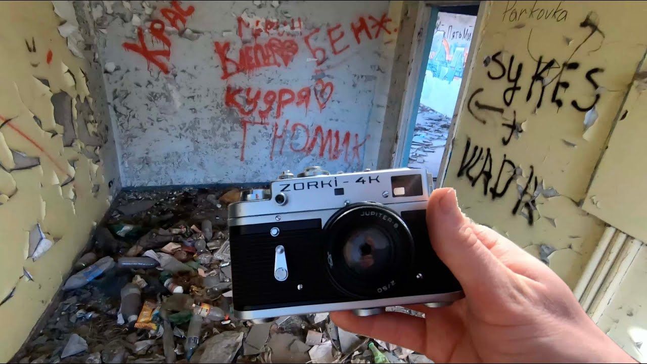A vintage film camera being held in front of graffiti-covered walls in an abandoned building.