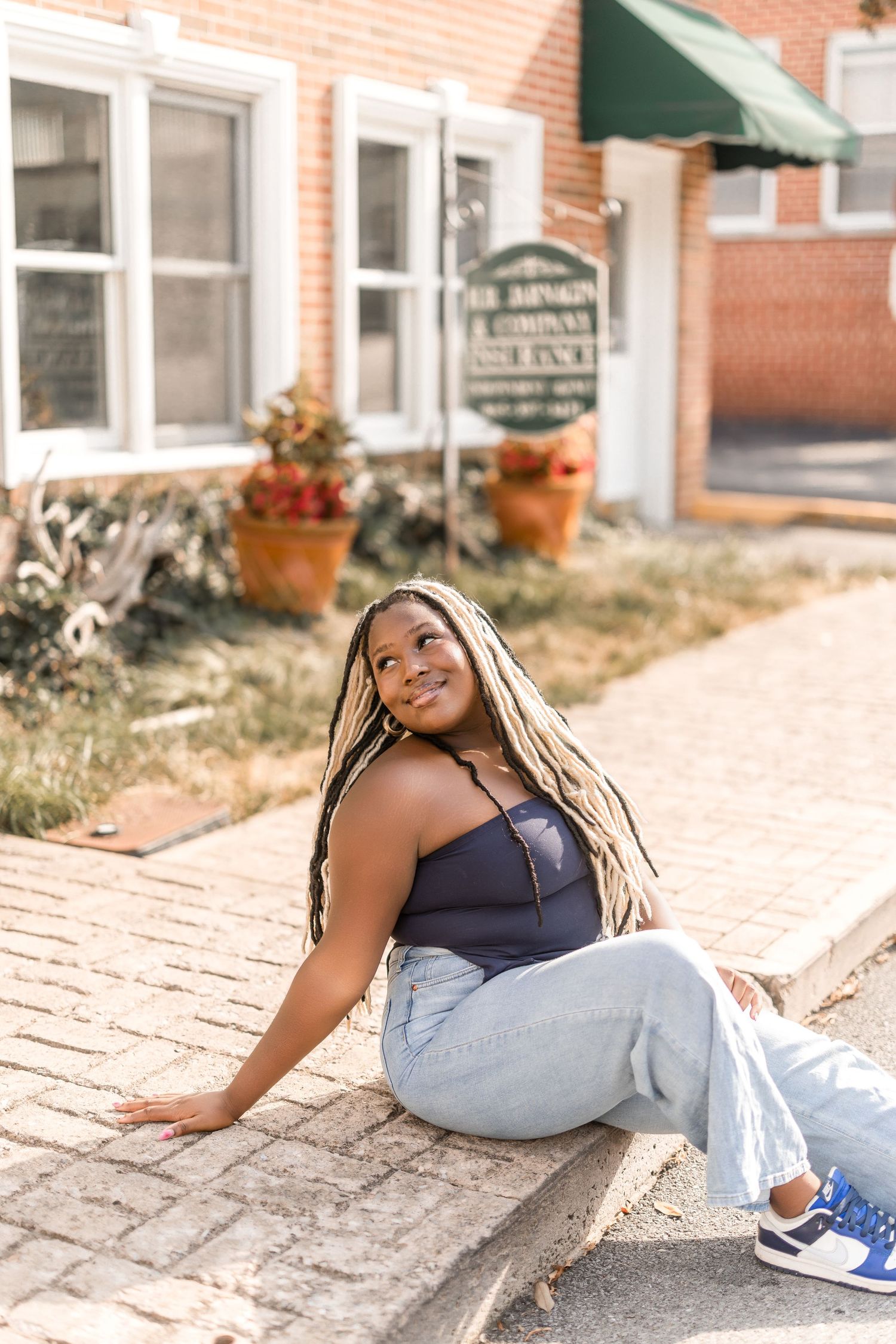 A person in casual attire lies on brick pavement while posing in natural sunlight during an outdoor photo session.