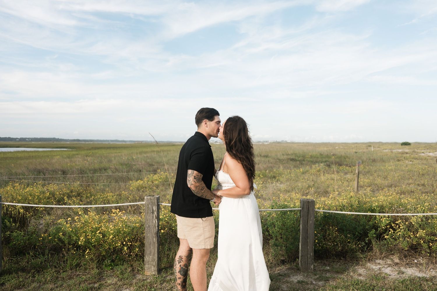 A couple embraces on a scenic overlook with vast grasslands and natural landscape stretching to the horizon.