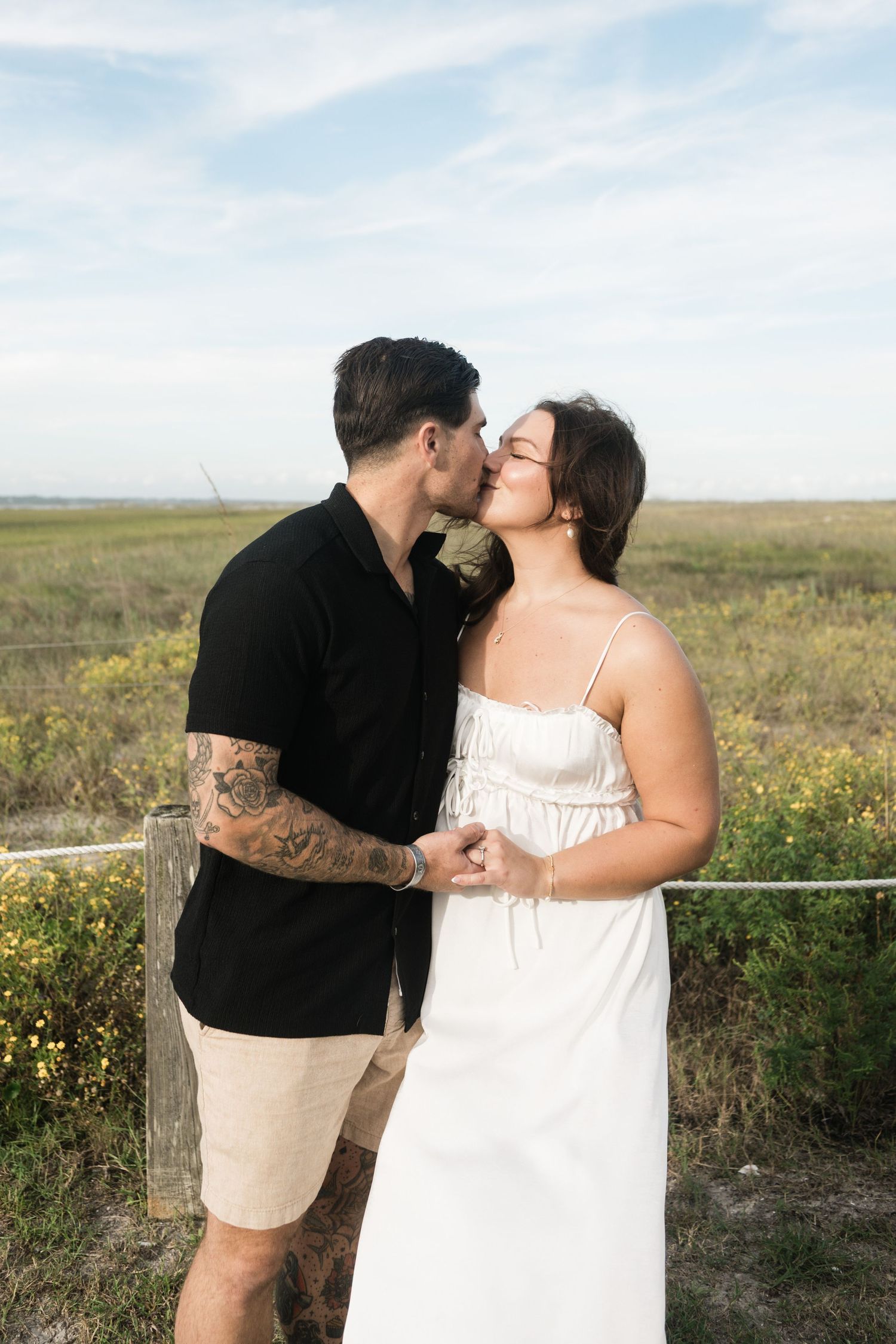 A romantic couple shares an intimate moment in a field of wildflowers against a soft blue sky.