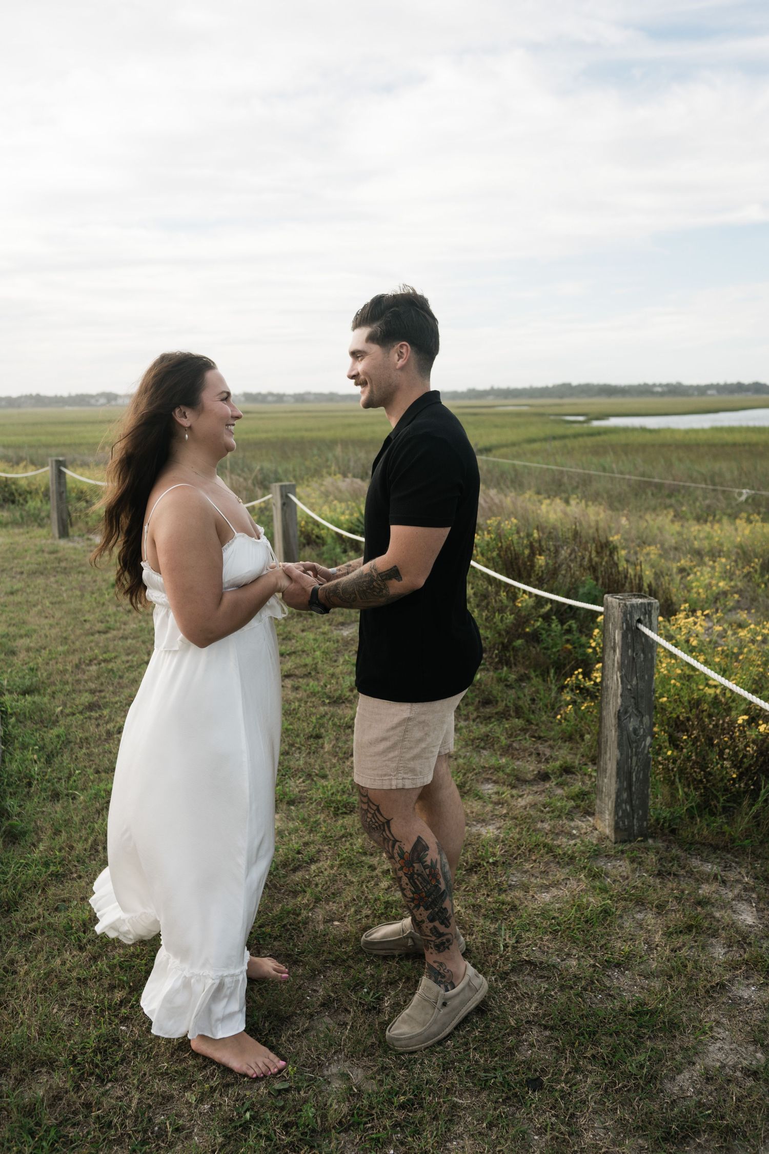 A couple shares a joyful moment together in a scenic field with rolling hills and wildflowers in the background.