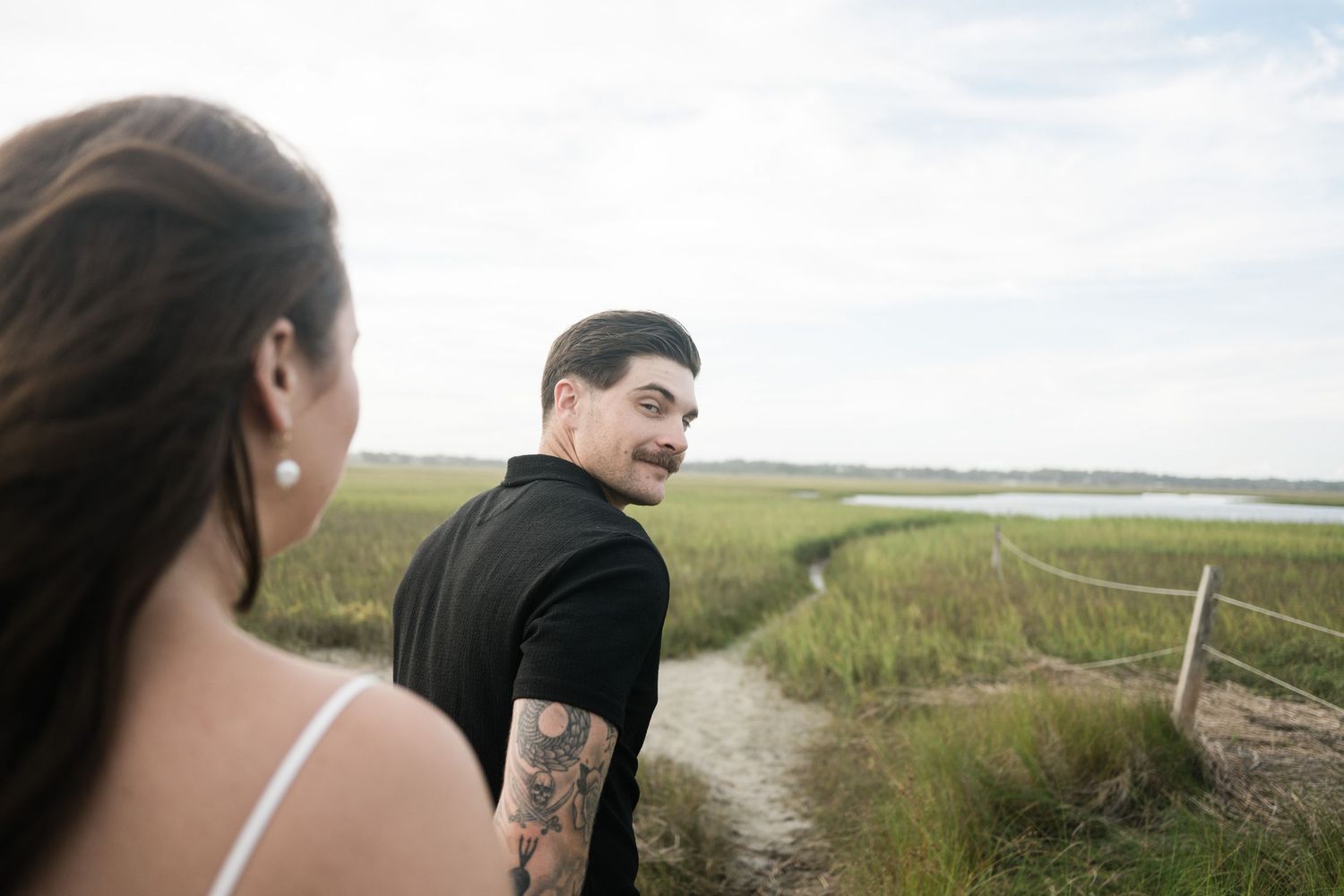 Two people strolling on a wooden walkway through coastal wetlands on a sunny afternoon.