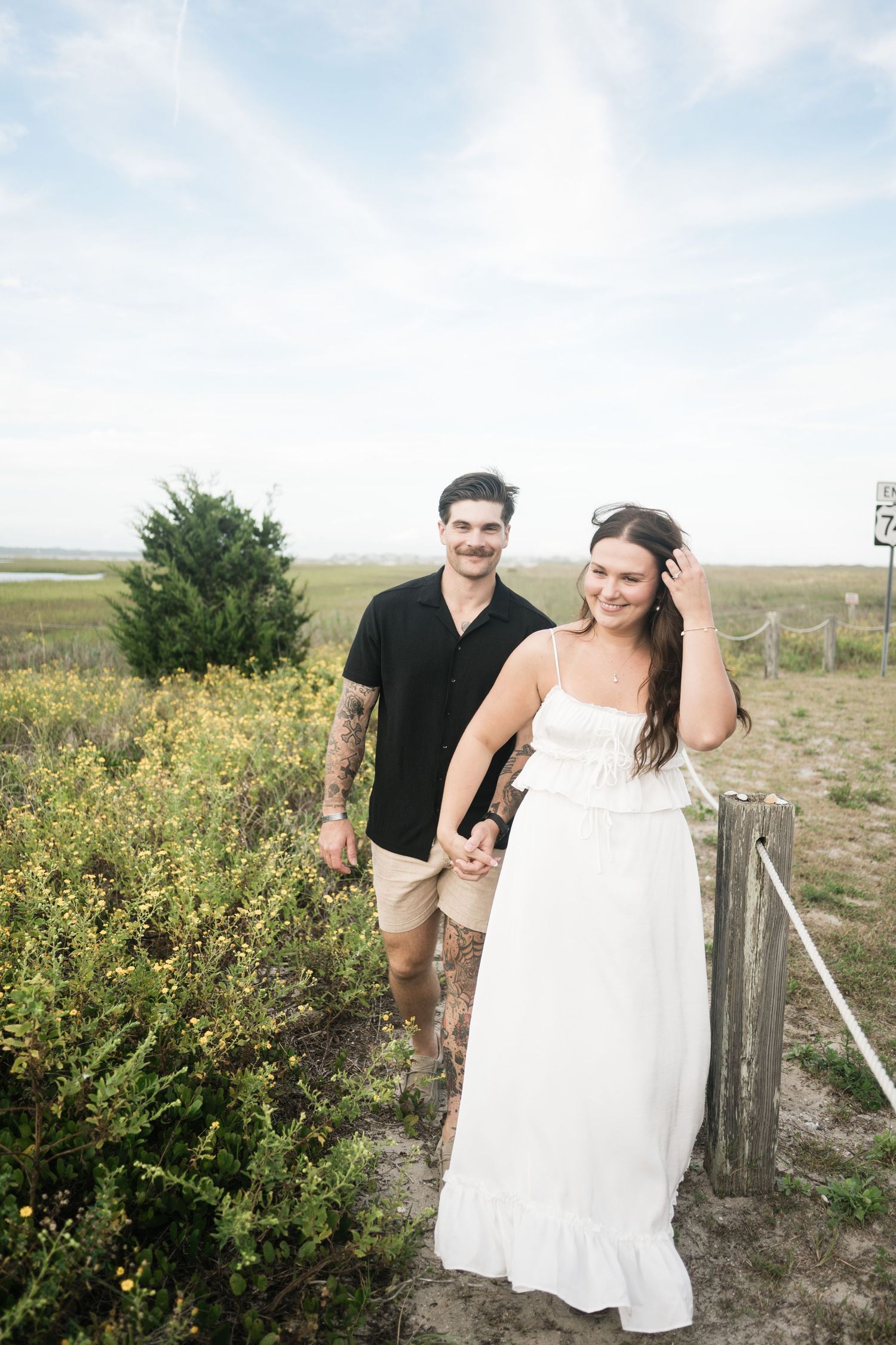 A couple poses together in a natural outdoor setting with greenery and open fields in the background.