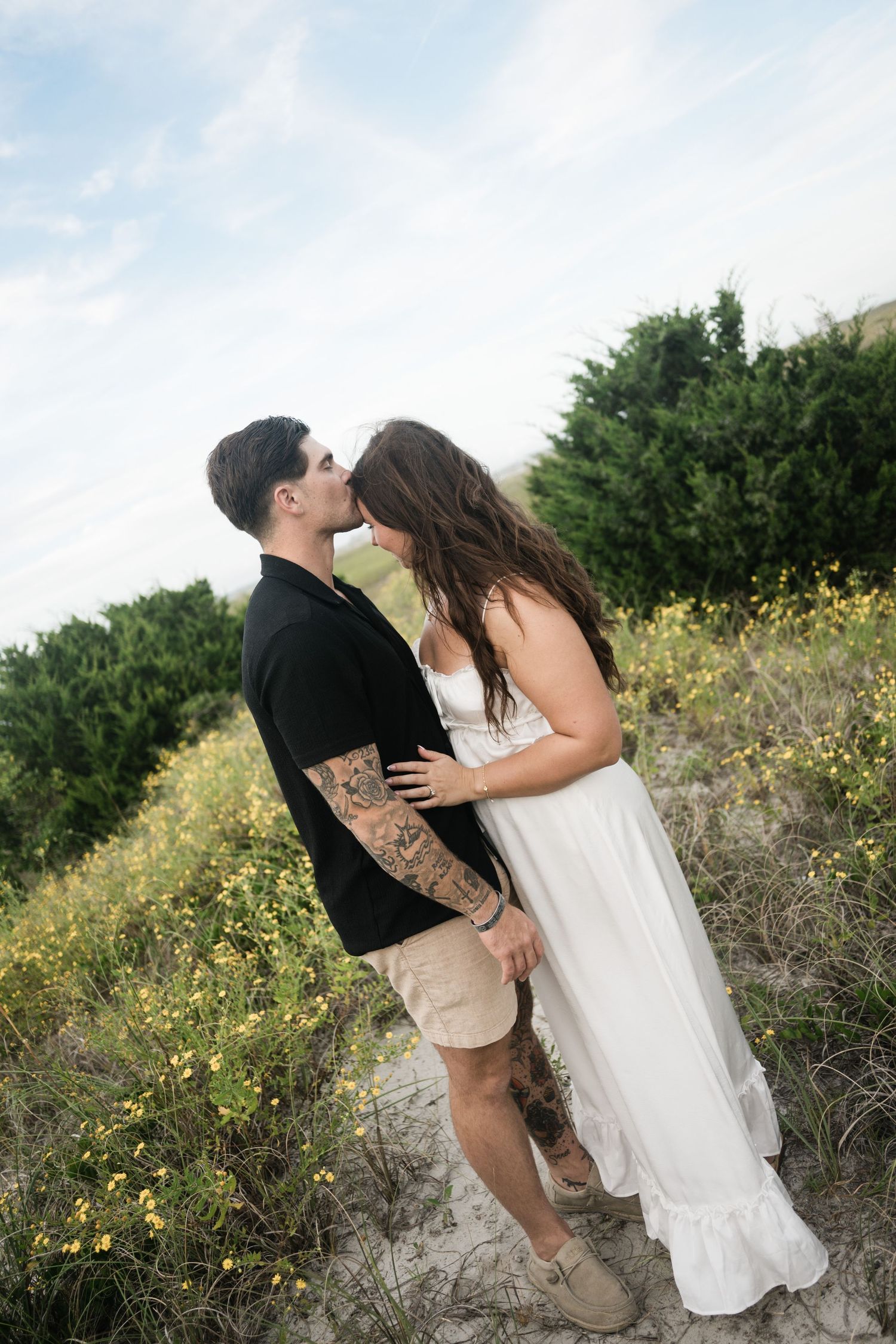 A couple embraces playfully in a coastal garden with yellow flowers blooming.