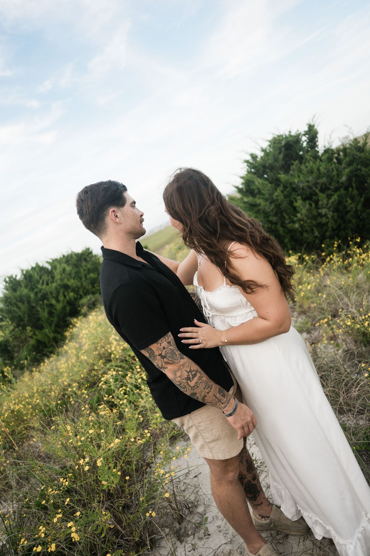 A couple shares intimate moments while surrounded by coastal vegetation and yellow blooms.