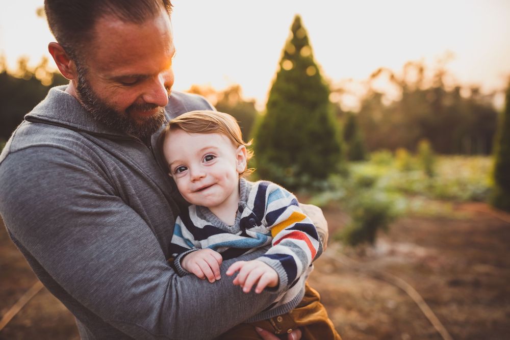Parent and child share a tender outdoor moment at sunset in a natural setting.
