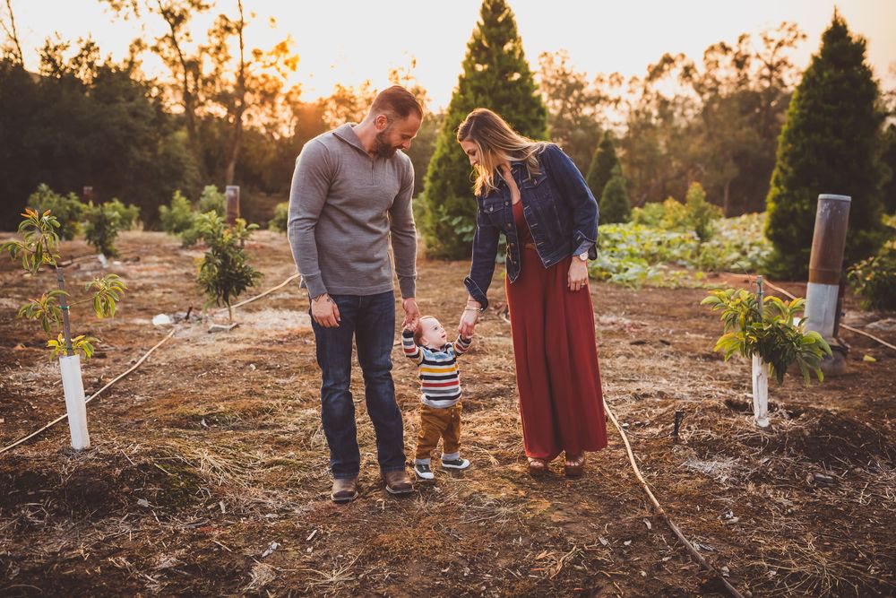 Family walking through a garden path at sunset with warm golden light filtering through trees.