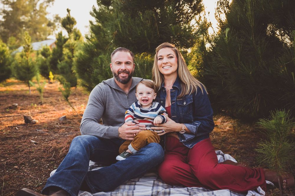 Family relaxing on a blanket among pine trees during an autumn sunset photoshoot.