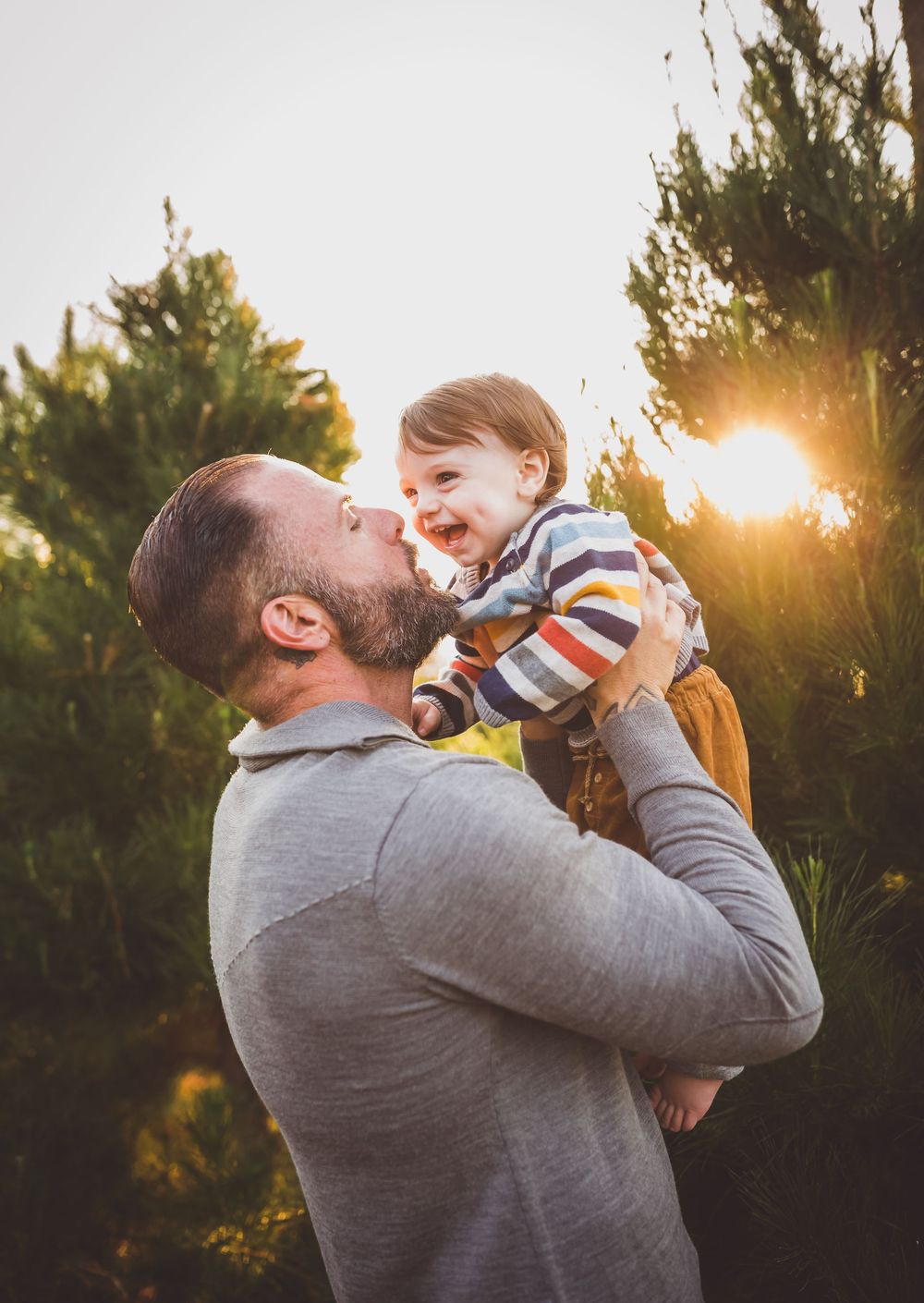 A tender moment between parent and child is captured at sunset with evergreen trees in the background.