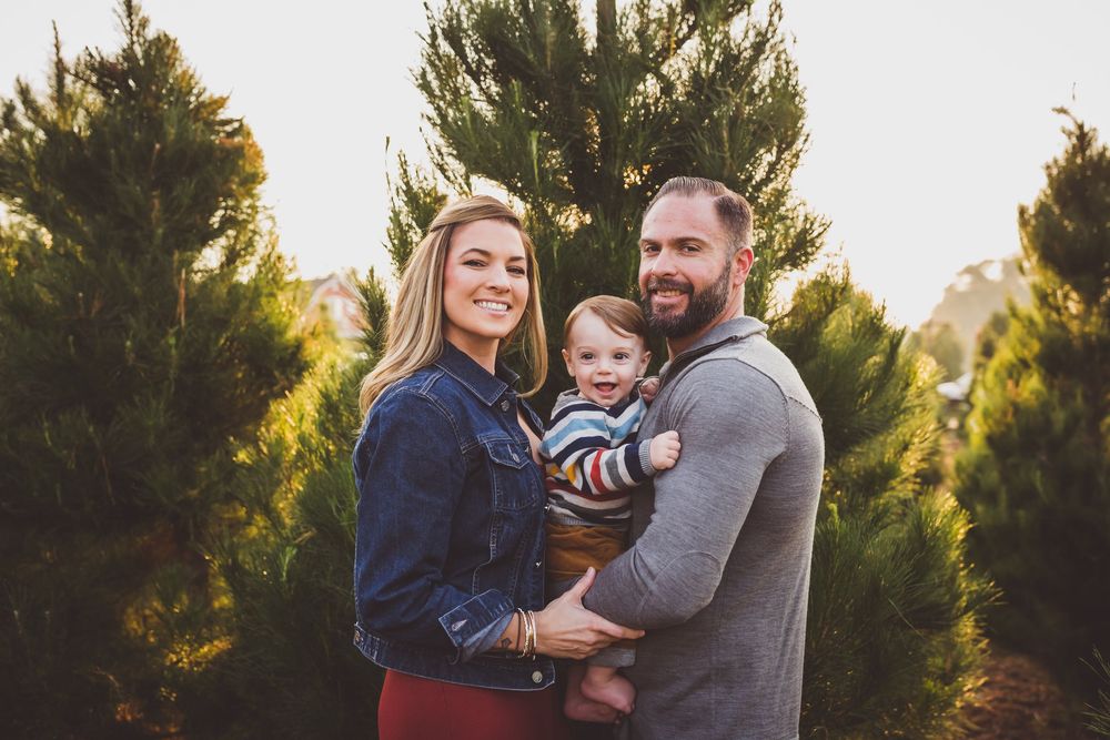 A family poses together outdoors among evergreen trees during a golden sunset photo session.