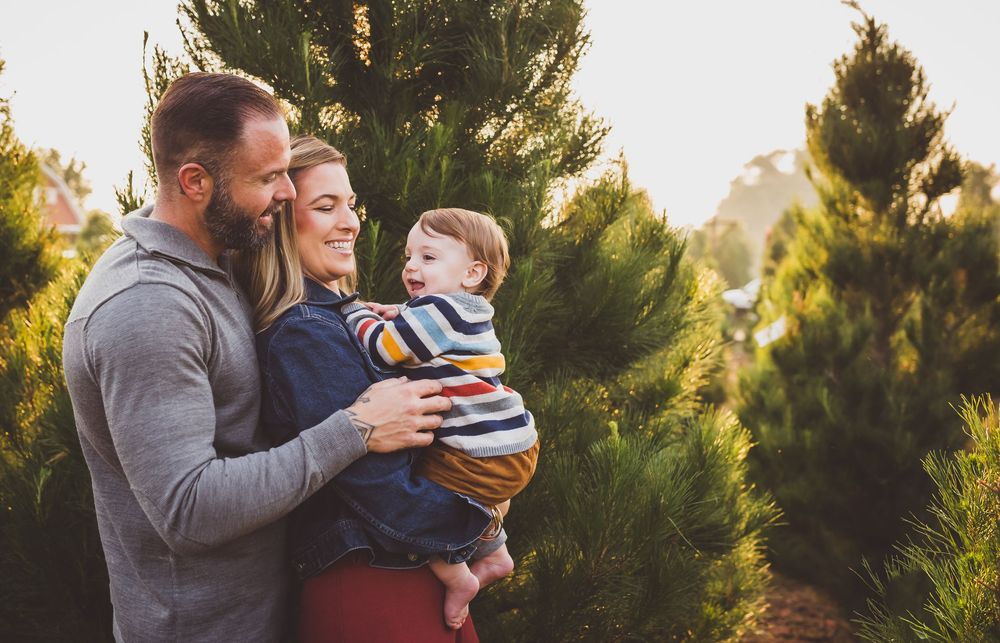 A family shares a tender moment together outdoors among evergreen trees during golden hour.