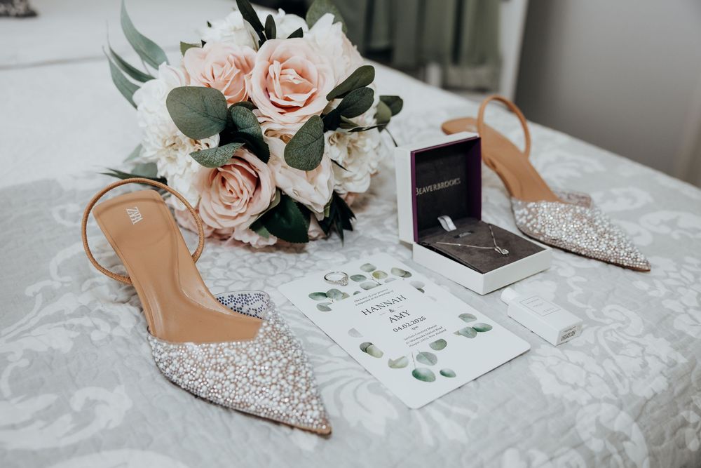 Elegant bridal accessories including sparkly heels and delicate pink roses arranged on white linen.