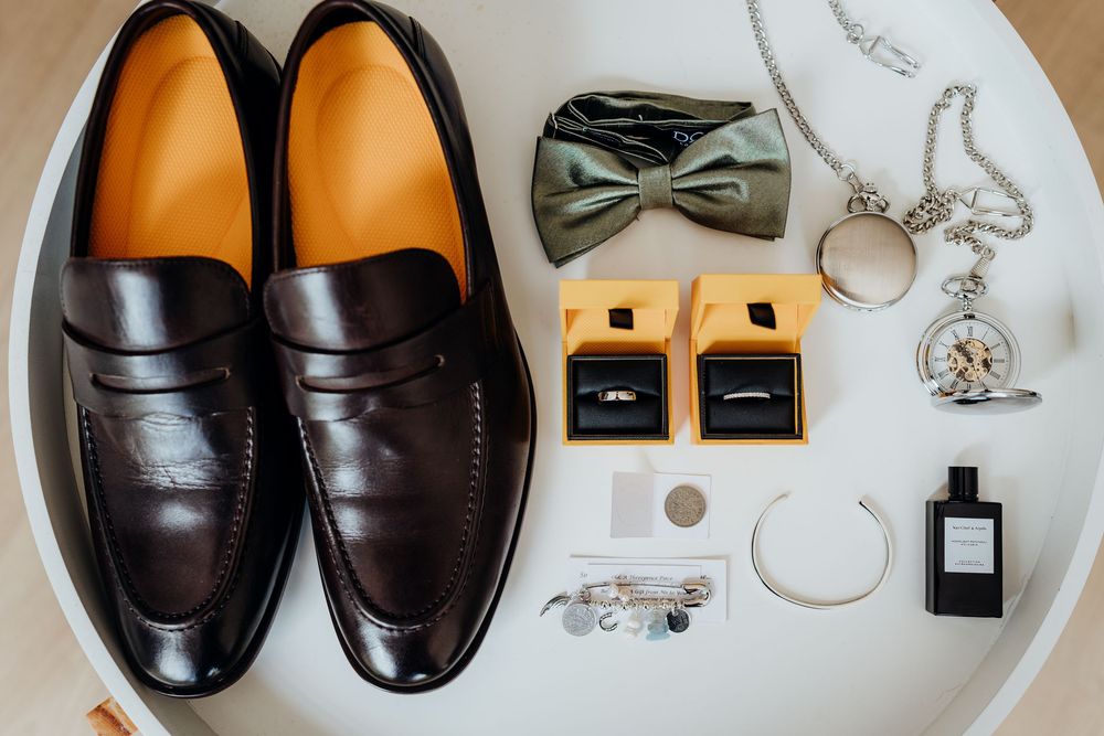 A collection of men's formal leather loafers and dress shoes arranged with accessories like bow ties and jewelry.