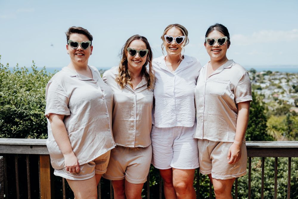 Group wearing coordinated white and beige summer outfits posing outdoors against scenic coastal backdrop.