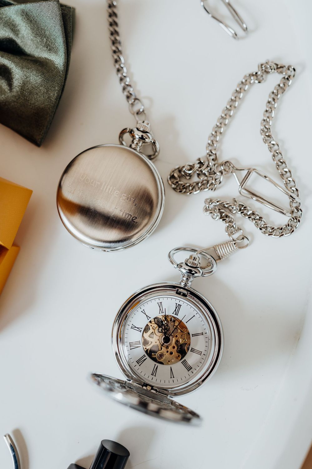 Silver pocket watch with chain displayed on white surface showing mechanical inner workings and roman numerals.