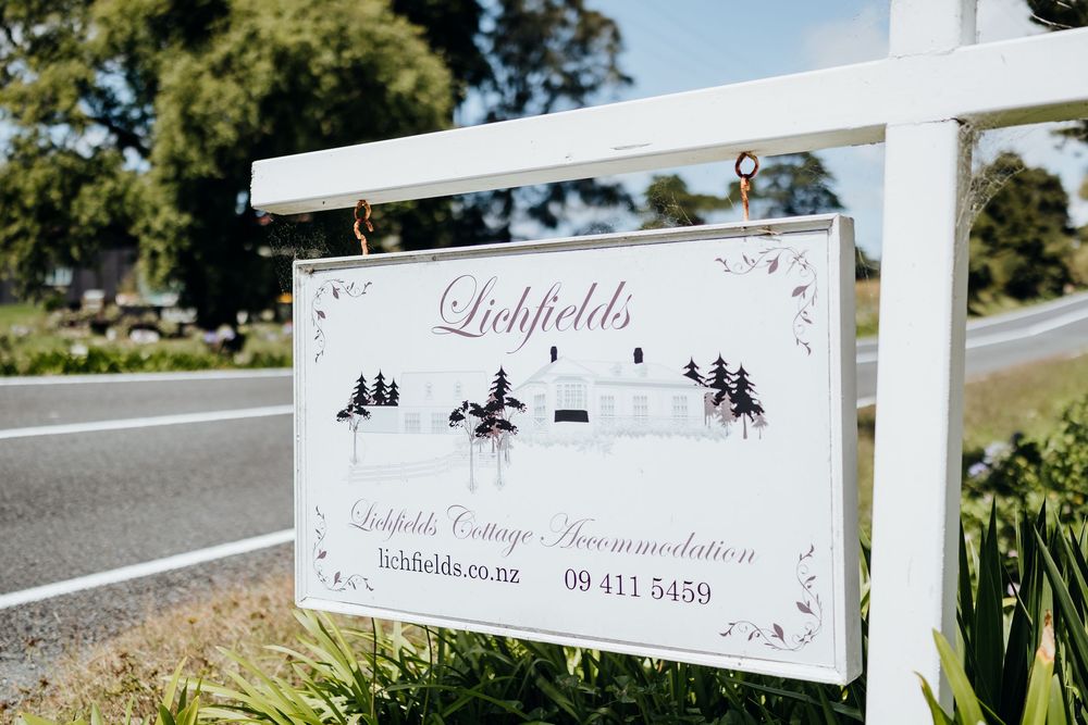 A white and gray property sign for Lichfields with decorative pine tree silhouettes mounted on a post by the road.