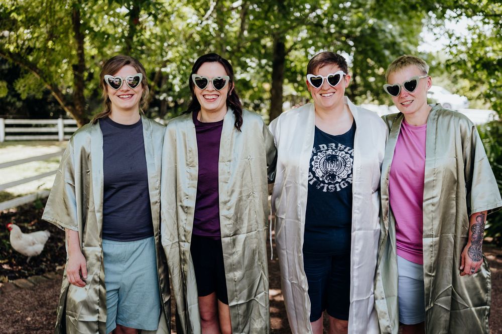 Group of wedding party members wearing sunglasses pose together outdoors on a sunny day.