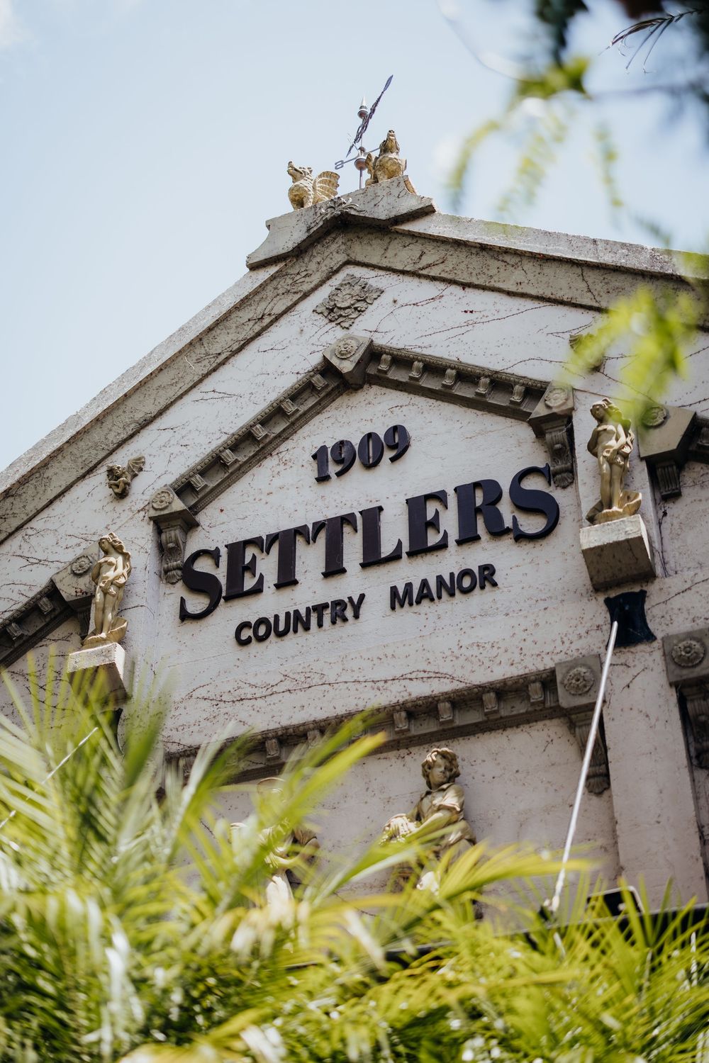 Vintage white sign reading 'Settlers Country Manor' mounted on an ornate architectural detail.