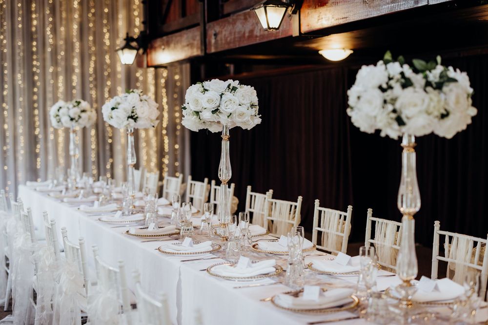 Luxurious wedding reception setup with white floral centerpieces and crystal chandeliers in an elegant ballroom.