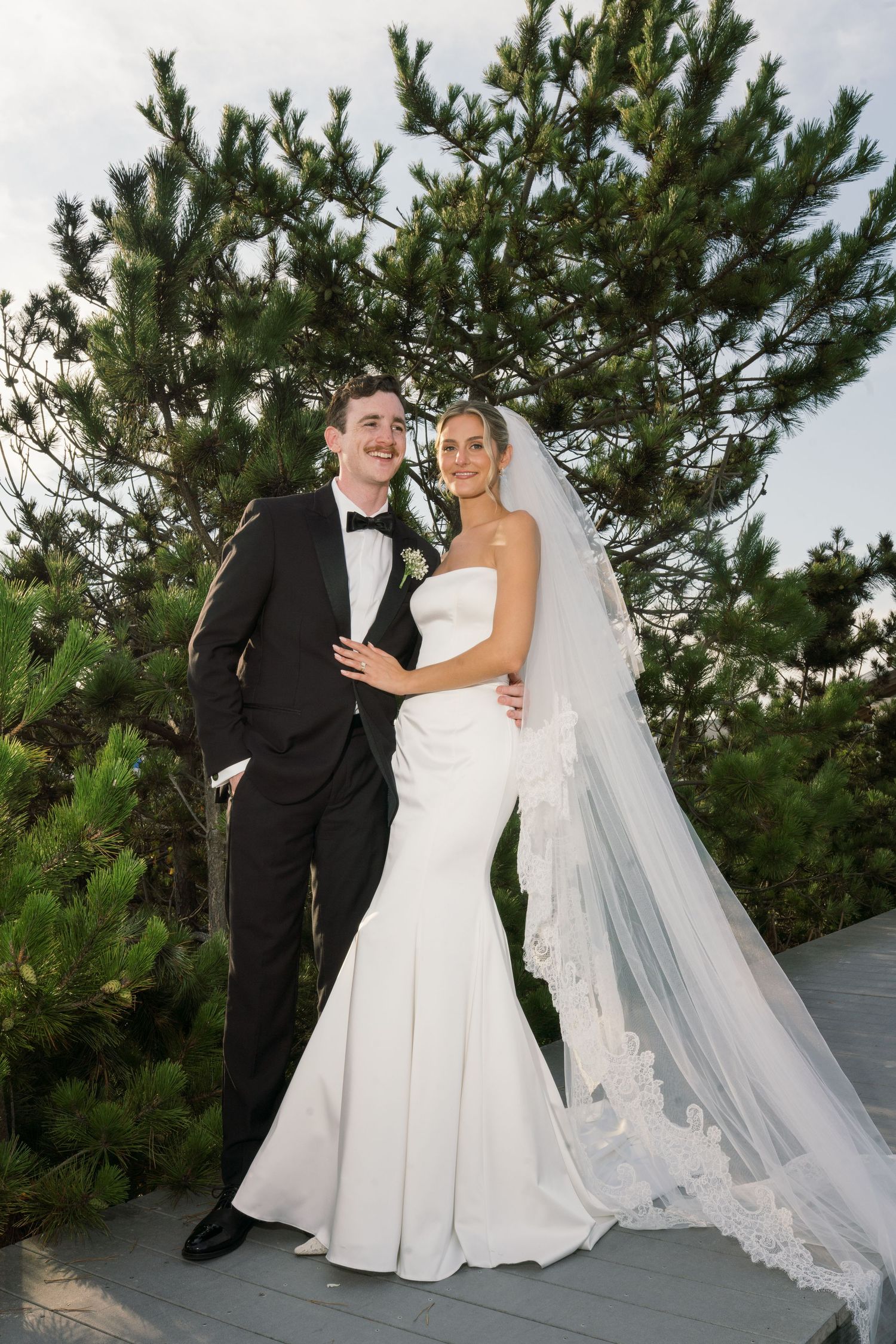 Newlyweds share an intimate moment among pine trees during their wedding photoshoot.