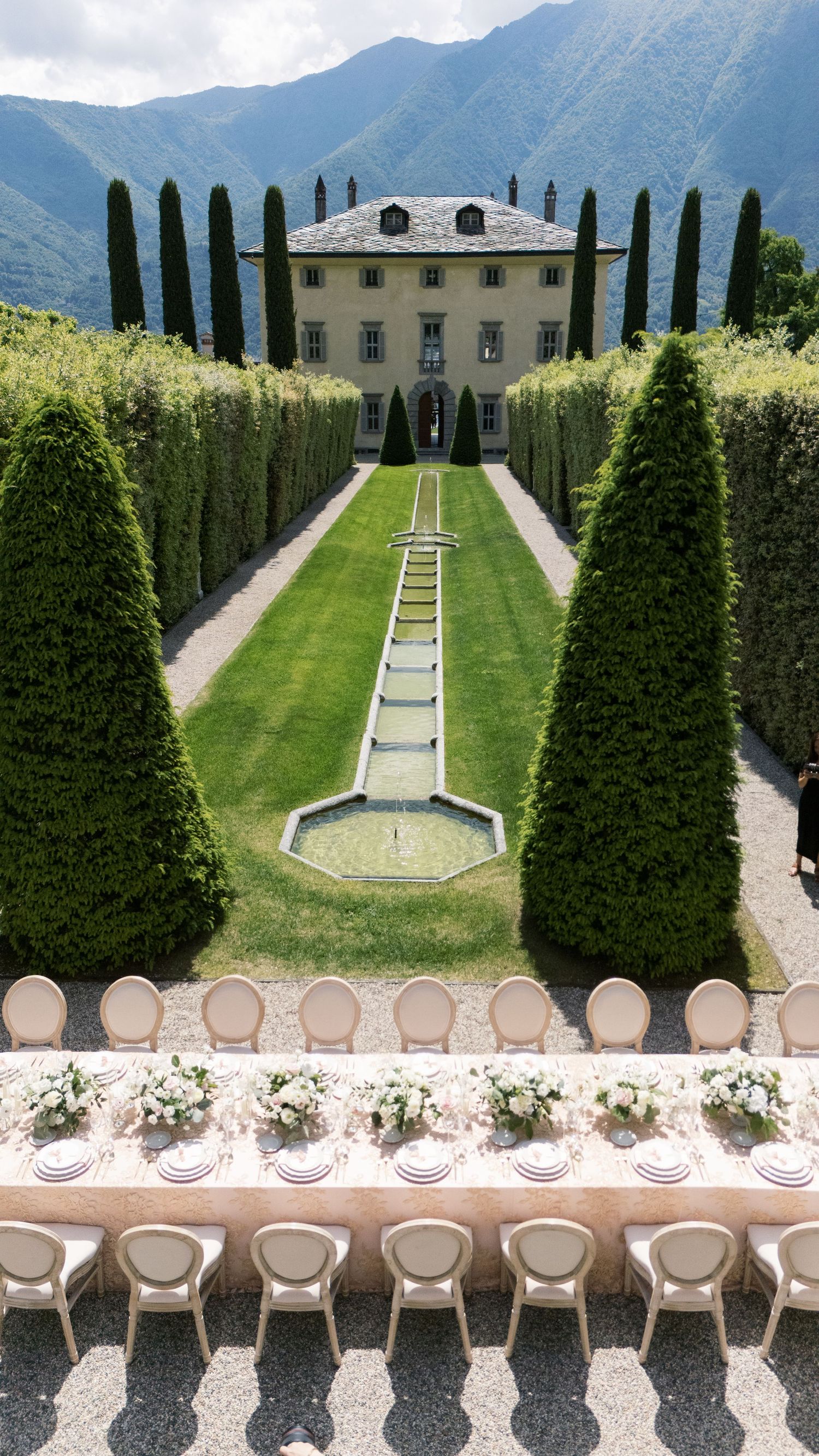 Italian villa wedding venue with cypress trees and mountain views along formal garden path.