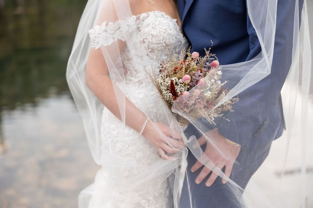 Couple in formal attire embracing with flowing white veil against mountain backdrop.