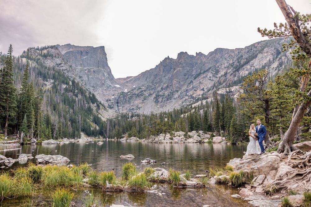 Mountain landscape with rocky peaks and alpine lake surrounded by evergreen forest.