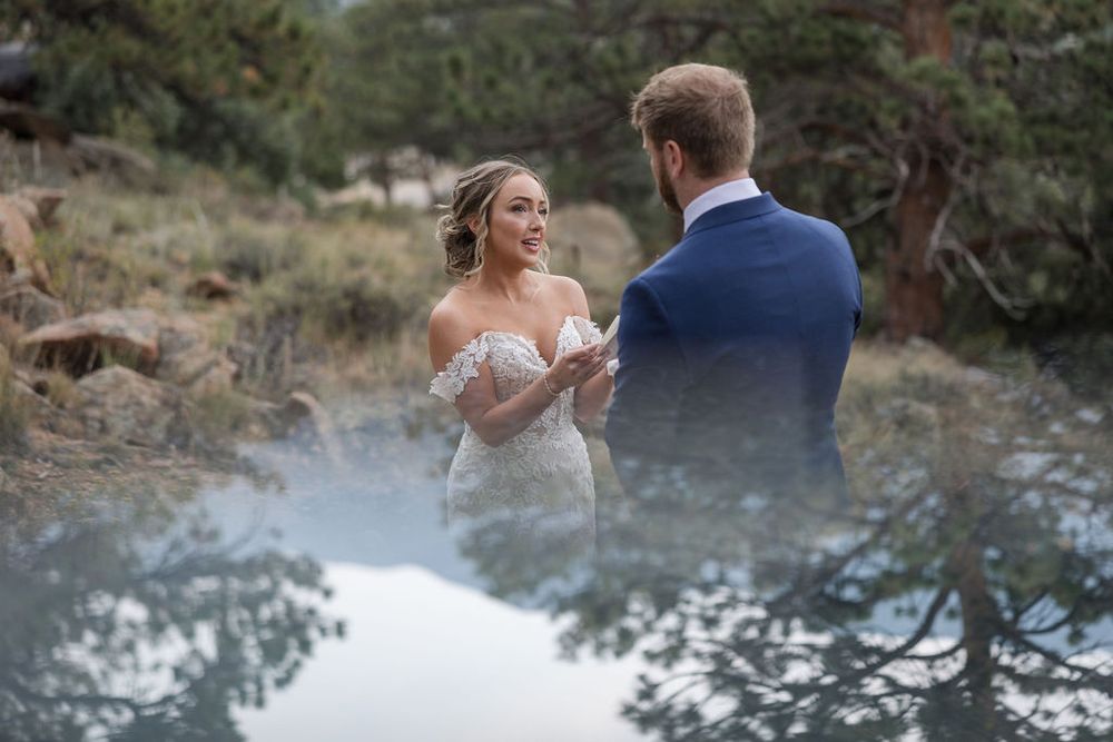 Newlyweds embrace during their outdoor mountain wedding with evergreen trees in the background.