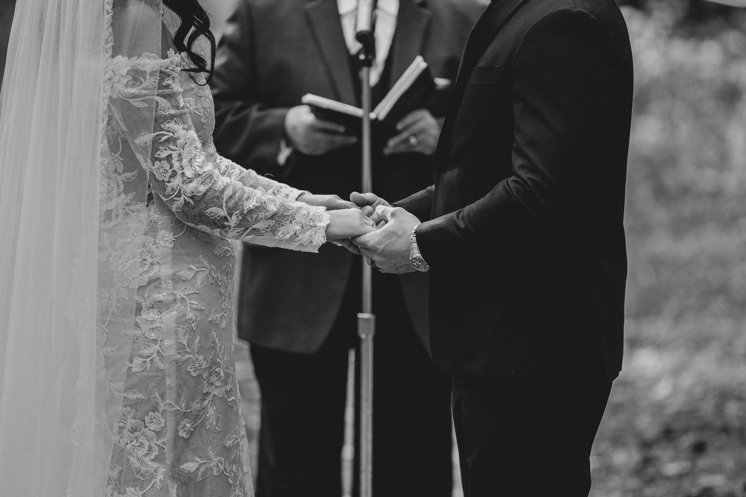 Wedding ceremony scene in black and white showing couple exchanging vows with officiant and guests.