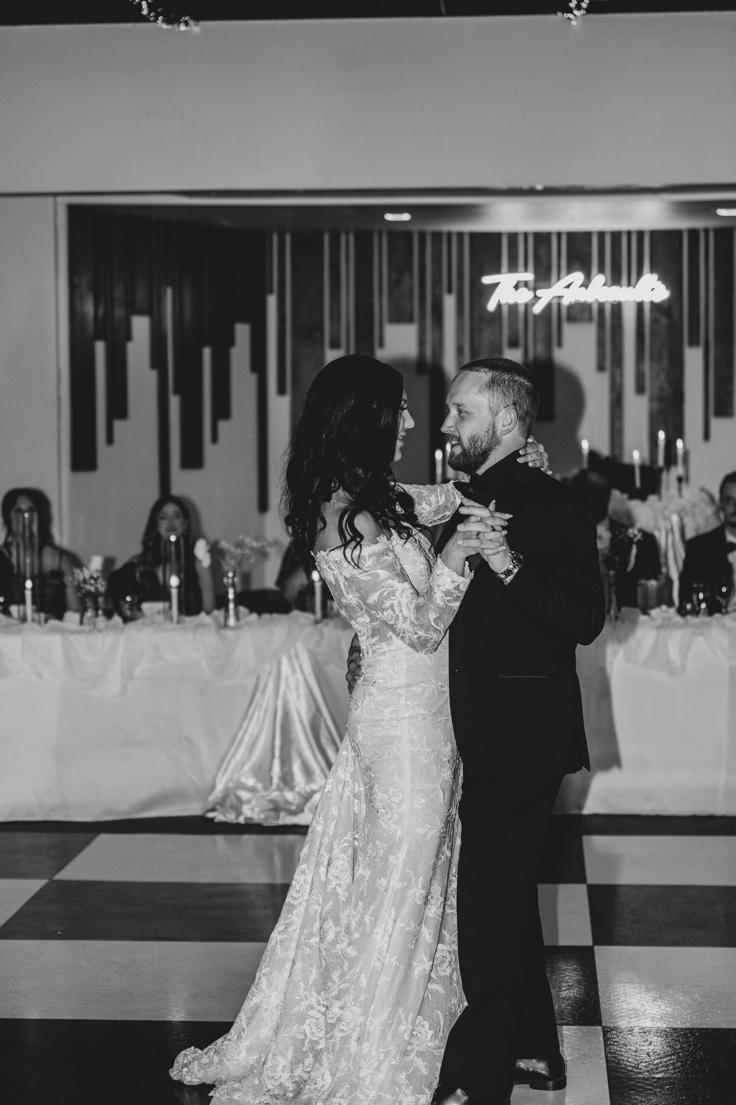 A couple dances together during a wedding reception in a beautifully decorated ballroom with white decor.