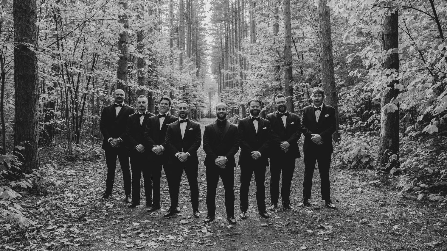 Panoramic black and white photo of wedding party lined up in a forest setting.