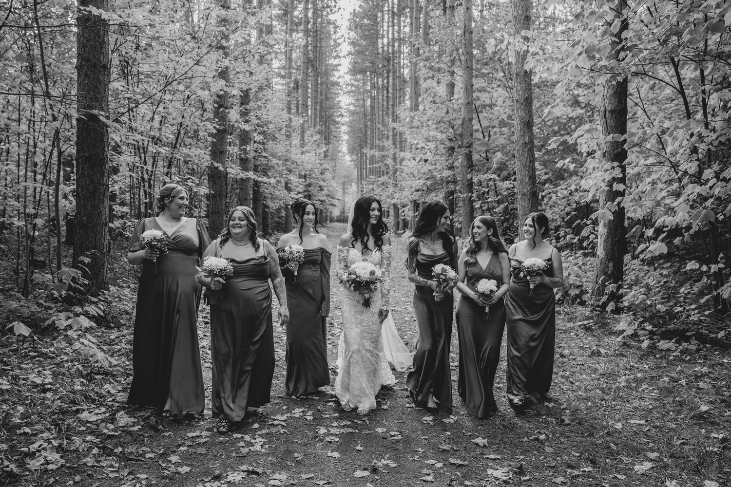 Panoramic black and white photo of wedding guests lined up in a wooded forest setting.