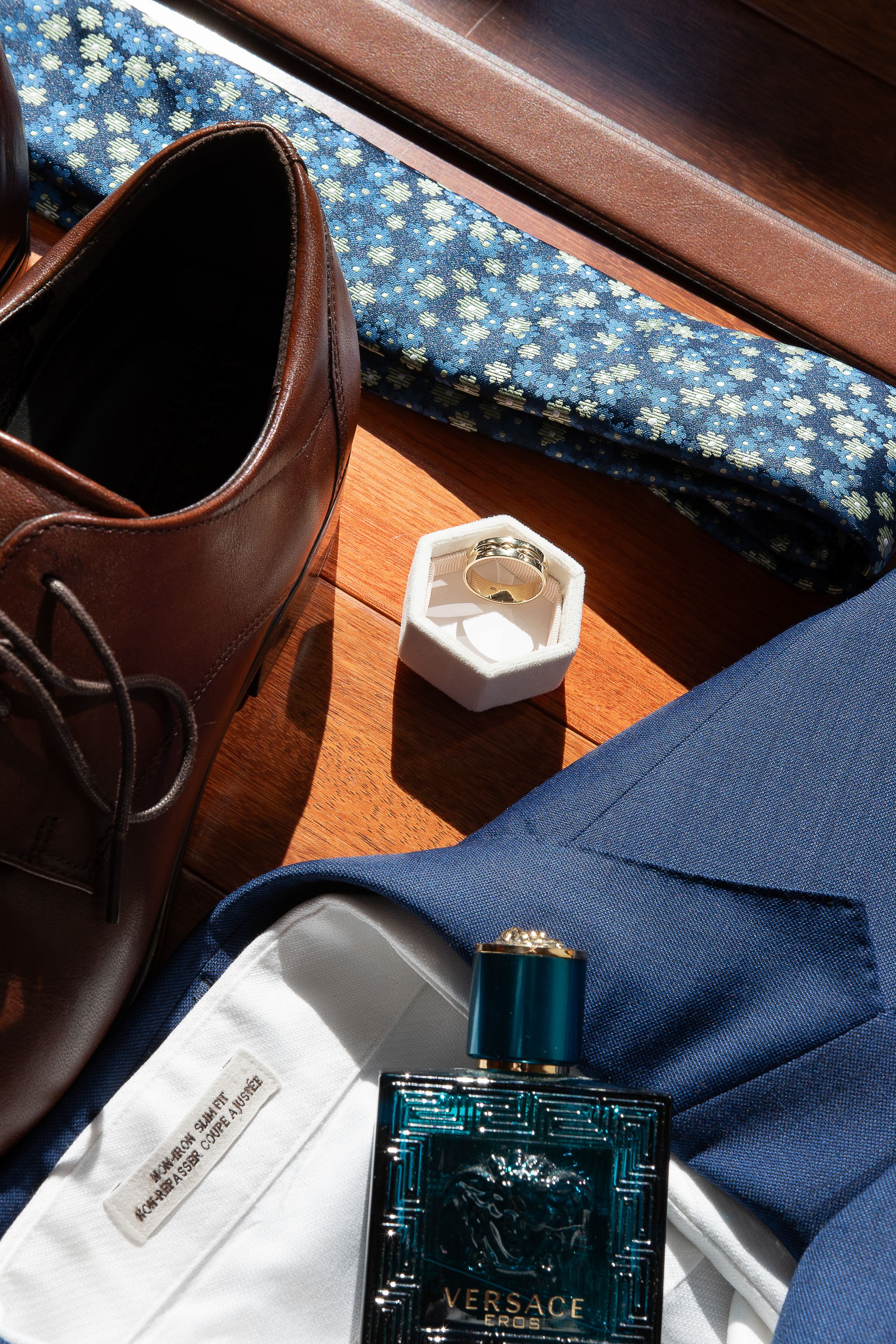 Blue floral wallpaper backdrop with a Versace perfume bottle and navy fabric on wooden surface.