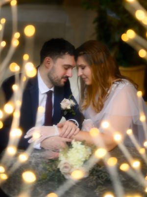 A romantic wedding couple embraces in a dimly lit setting with twinkling bokeh lights creating a magical atmosphere.