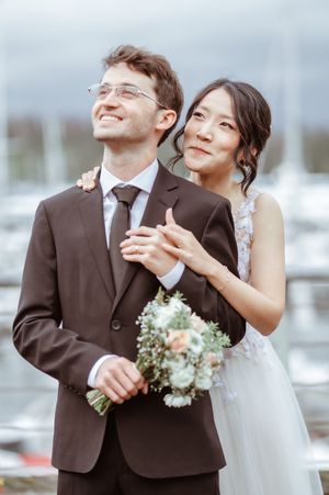 A couple in wedding attire shares a joyful moment together while looking upward in a romantic outdoor setting.