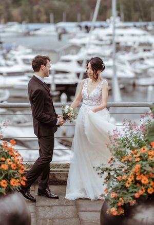 A romantic wedding couple shares a sweet moment by a marina with orange flowers and boats in the background.