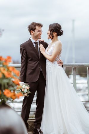 A romantic wedding couple shares tender moments on a balcony with orange flowers in the background.