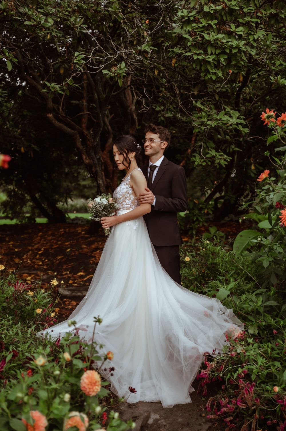 Romantic garden wedding portraits showing couple dancing and embracing among lush greenery and blooming flowers.