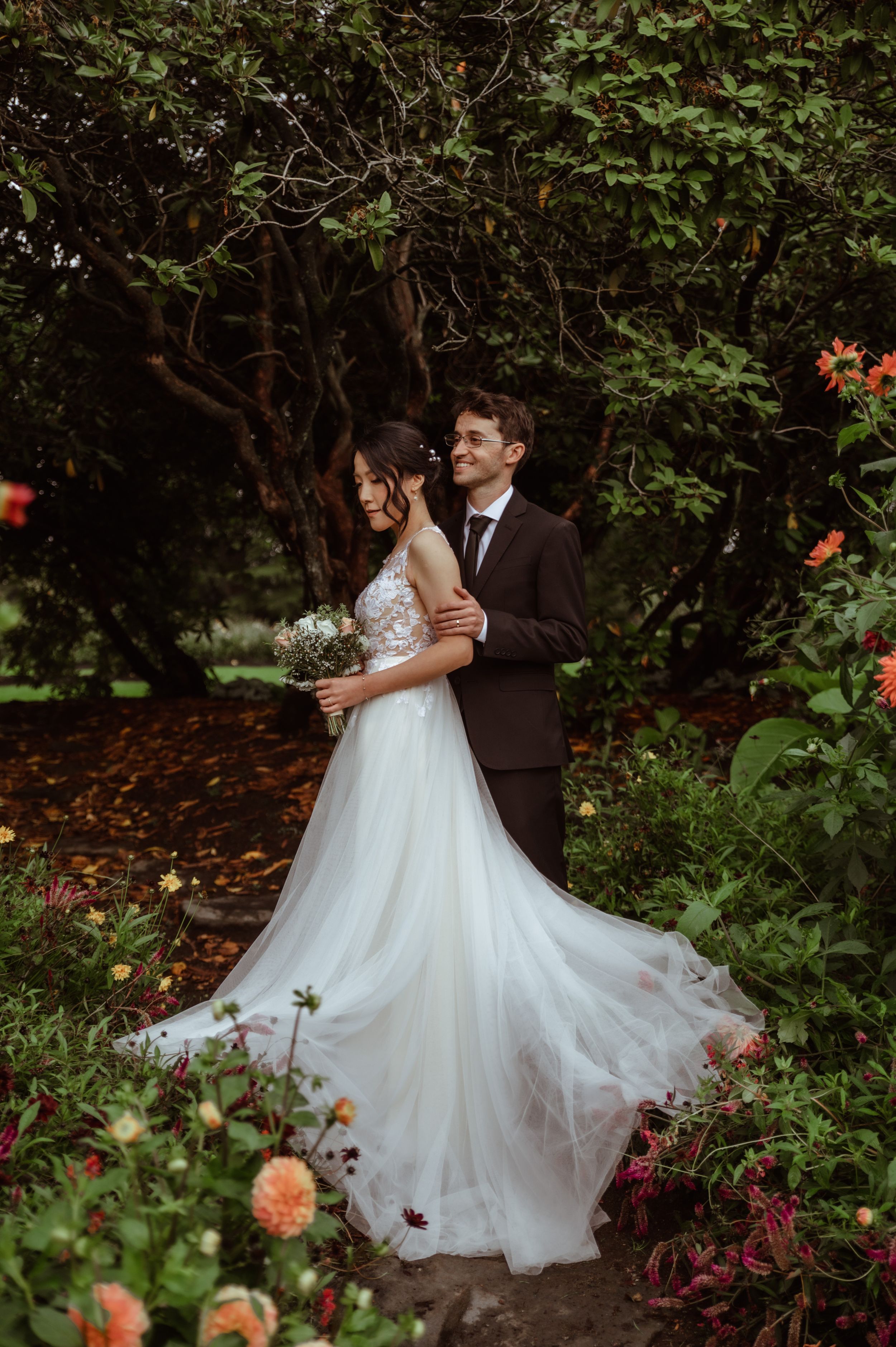 Romantic garden wedding portraits showing couple dancing and embracing among lush greenery and blooming flowers.