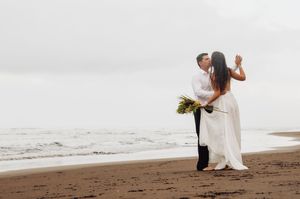 A couple in wedding attire shares an intimate moment on a misty beach at sunset.