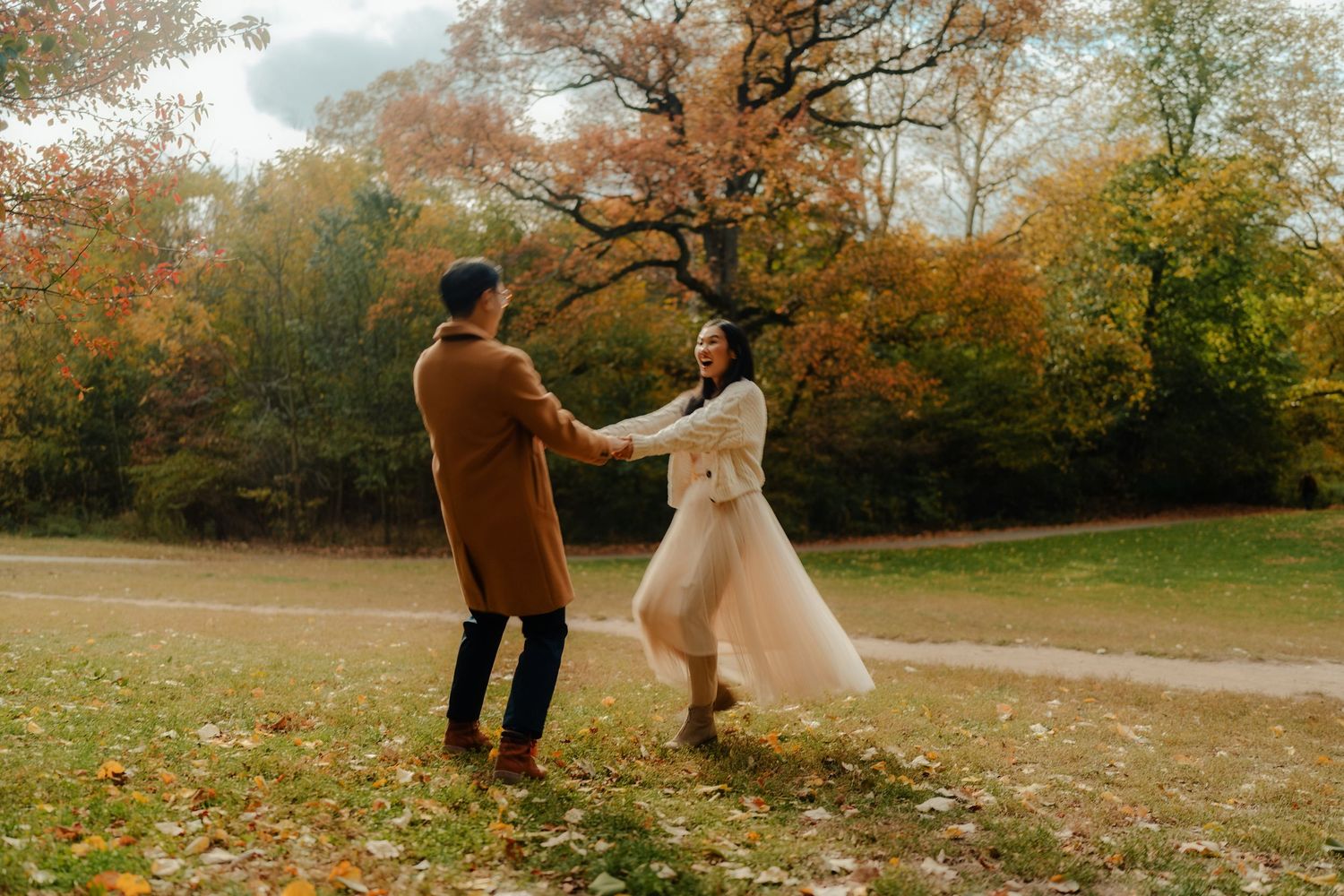 A couple in wedding attire walks through a scenic autumn park with vibrant orange and red fall foliage.