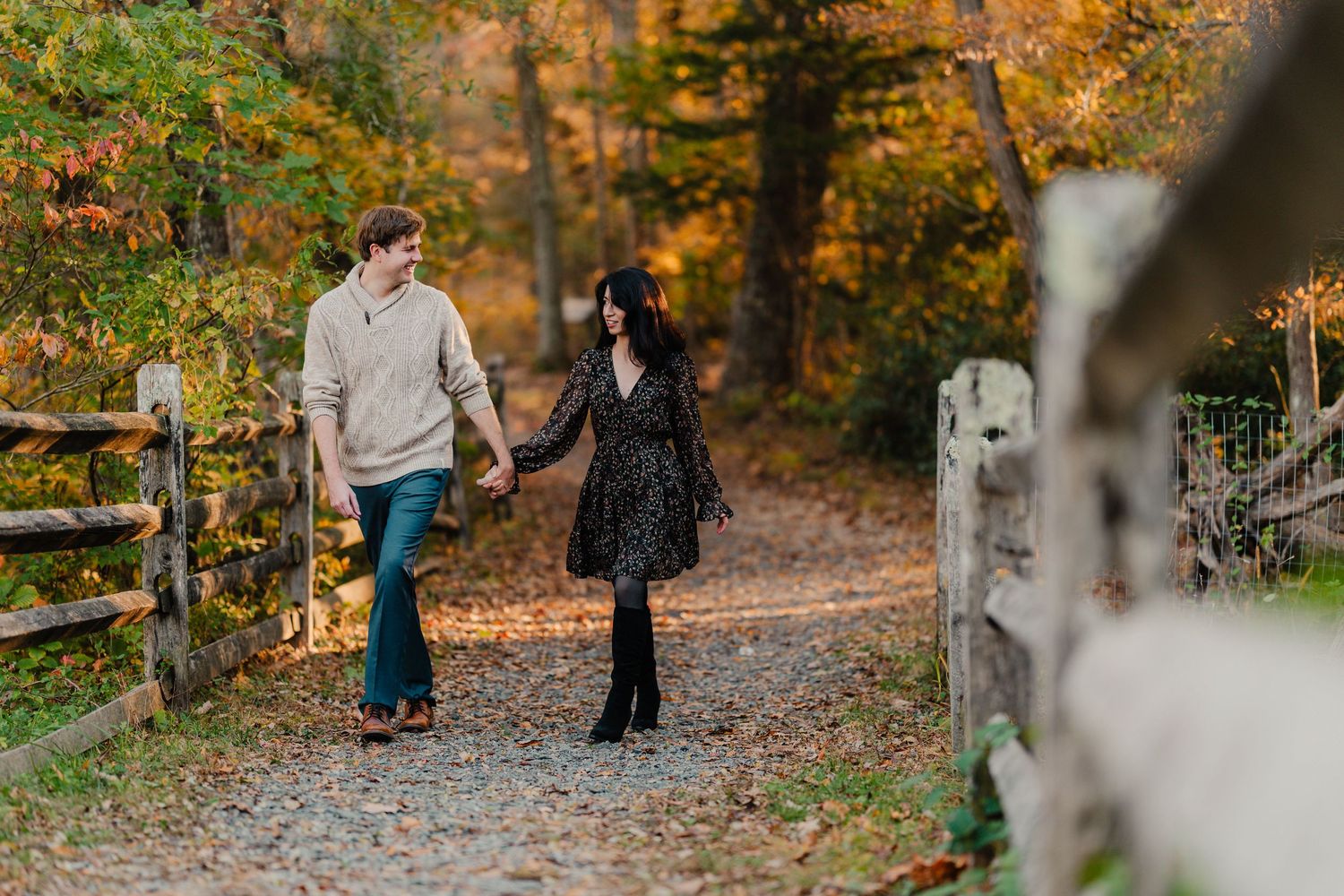 A couple walking together on a leaf-covered path through a vibrant autumn forest during a photo session.