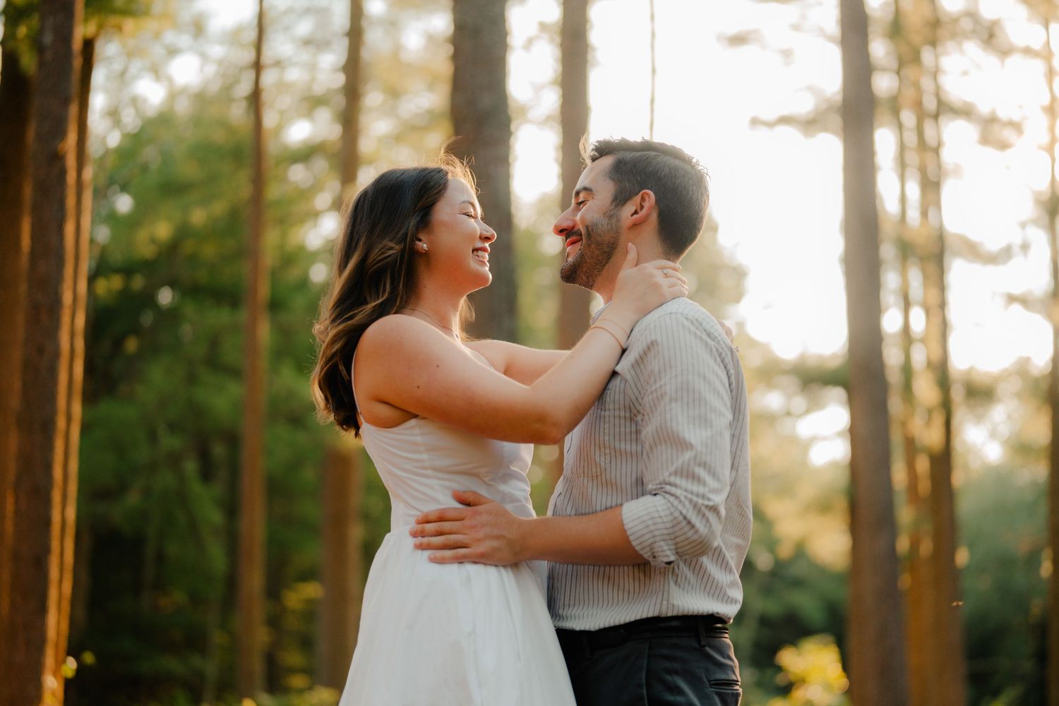 A couple shares a romantic moment while dancing together in a sunlit forest setting at golden hour.