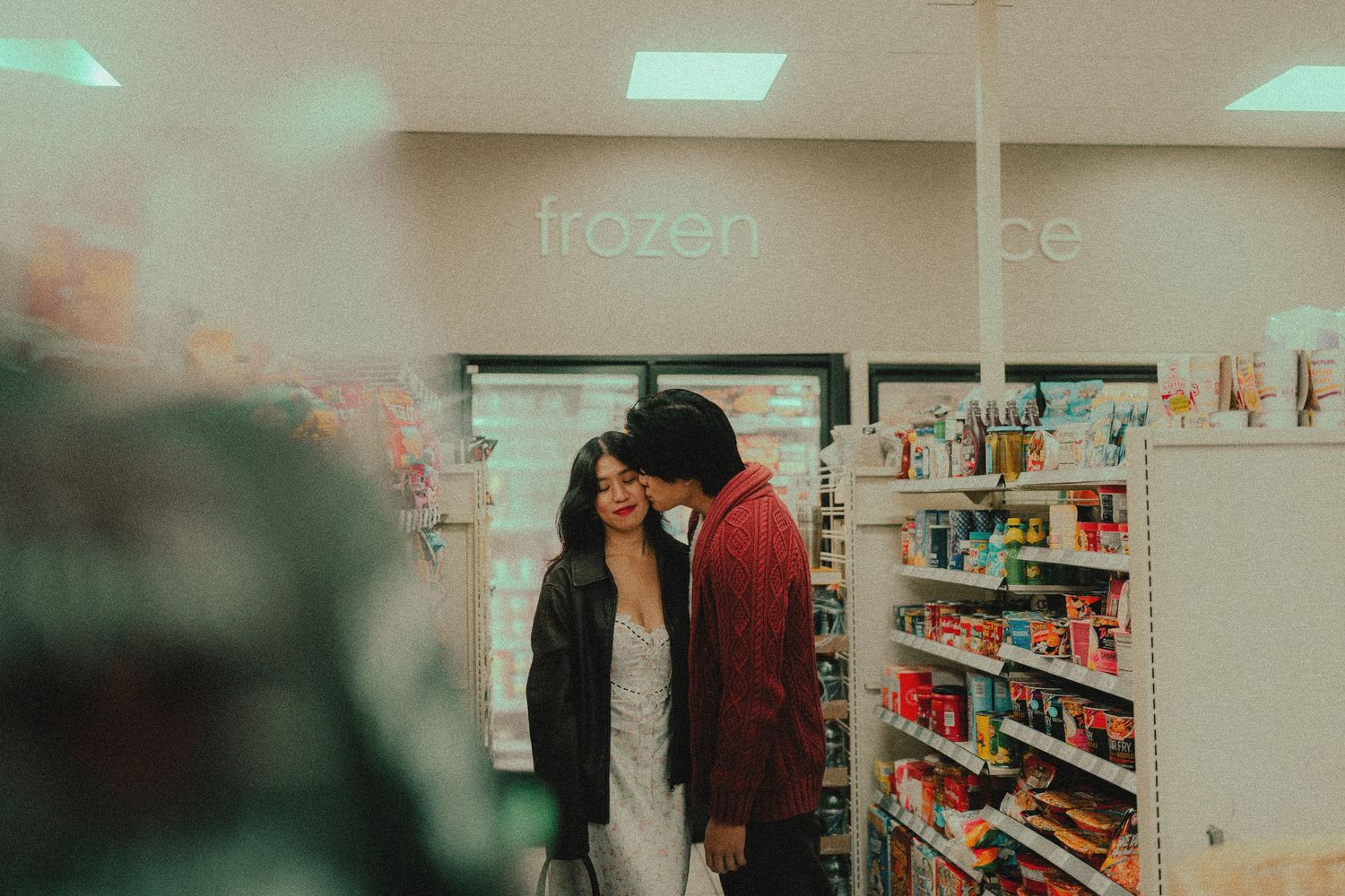 Couple sharing a romantic moment in a convenience store aisle near the frozen food section.