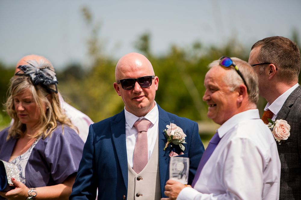 Wedding guests in formal attire socialize during outdoor summer reception.