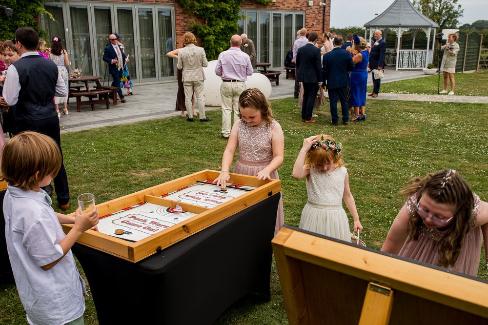 Wedding guests enjoying a fun lawn game with yellow balls and wooden ramps at an outdoor reception.