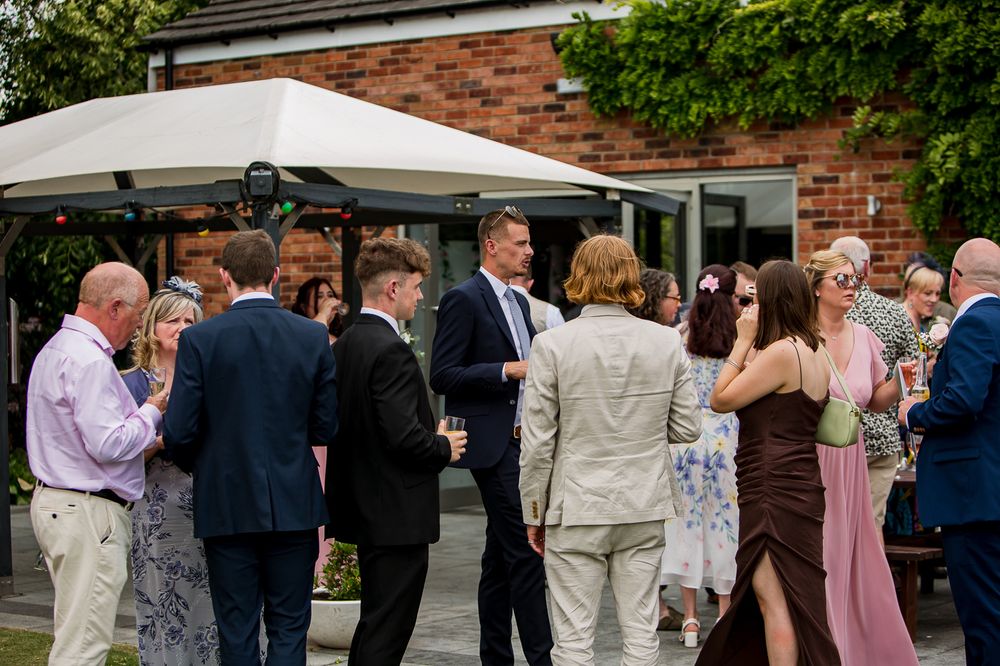 Wedding guests mingling outdoors near a brick building during a reception celebration.