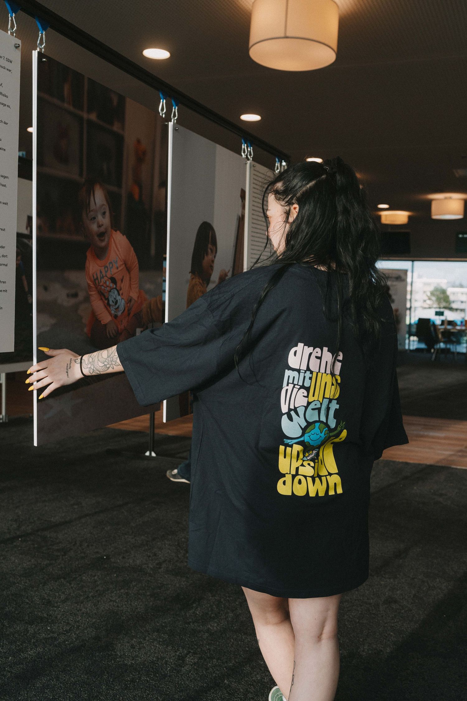 Person wearing black graphic t-shirt dress in indoor venue.